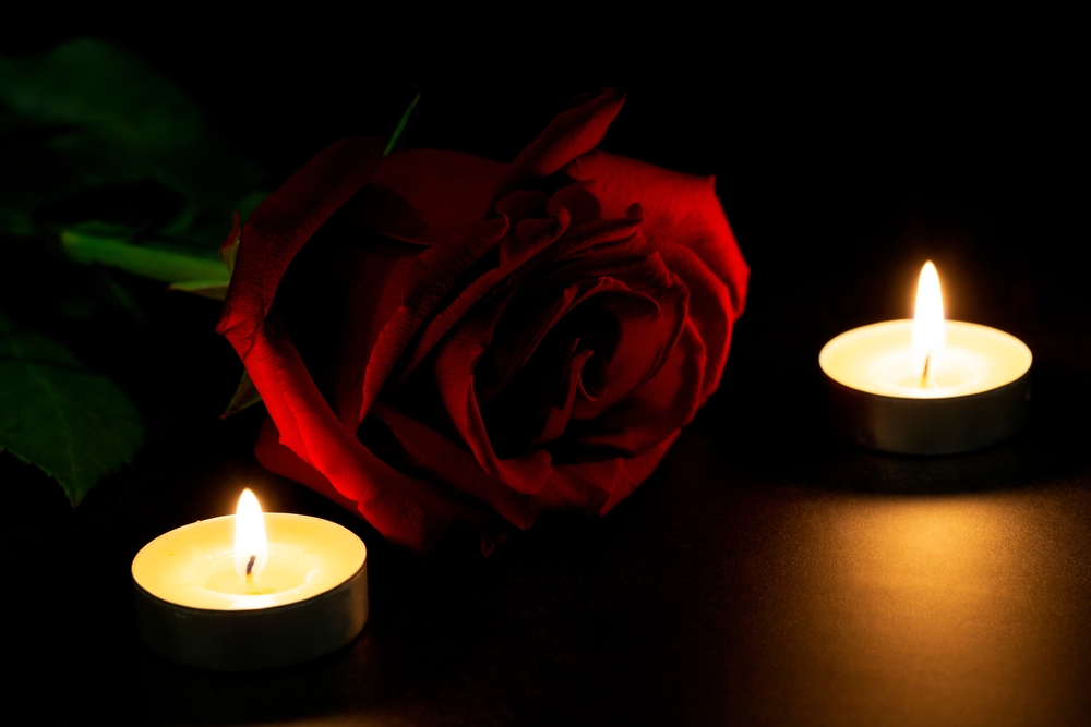 Red rose in between tea candles in dark room