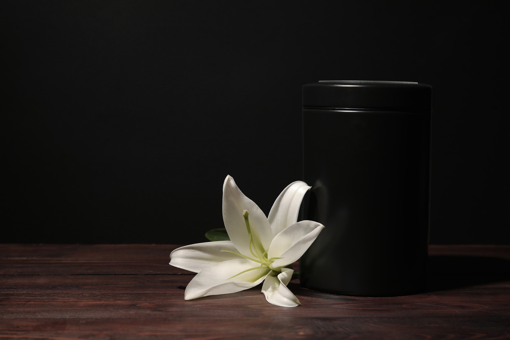 A mortuary urn and white lily on top of a dark wooden table
