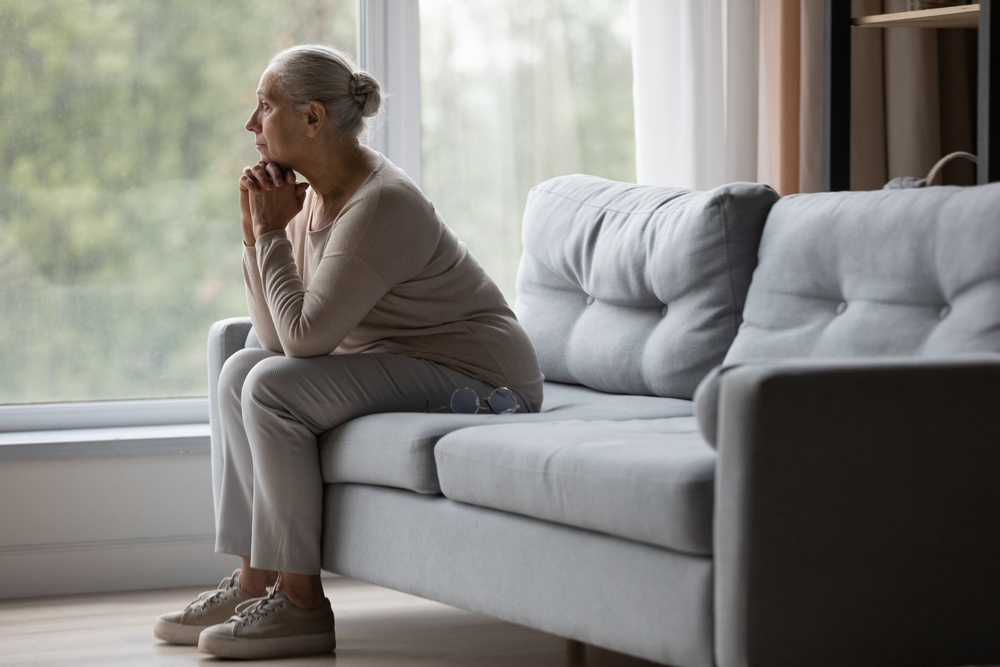 A woman sits alone on her couch staring out the window 