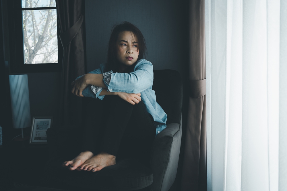 A woman sitting with her knees up on am armchair looking depressed and lost