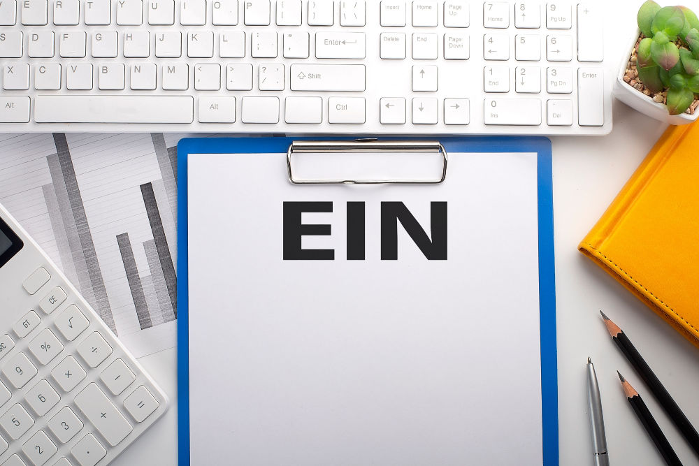 A clipboard with a page containing the term 'EIN' placed on a desk, along with a computer keyboard, calculator, pens, notebook.