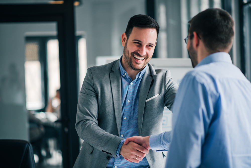 Business man shaking another employee's hand and smiling cordially