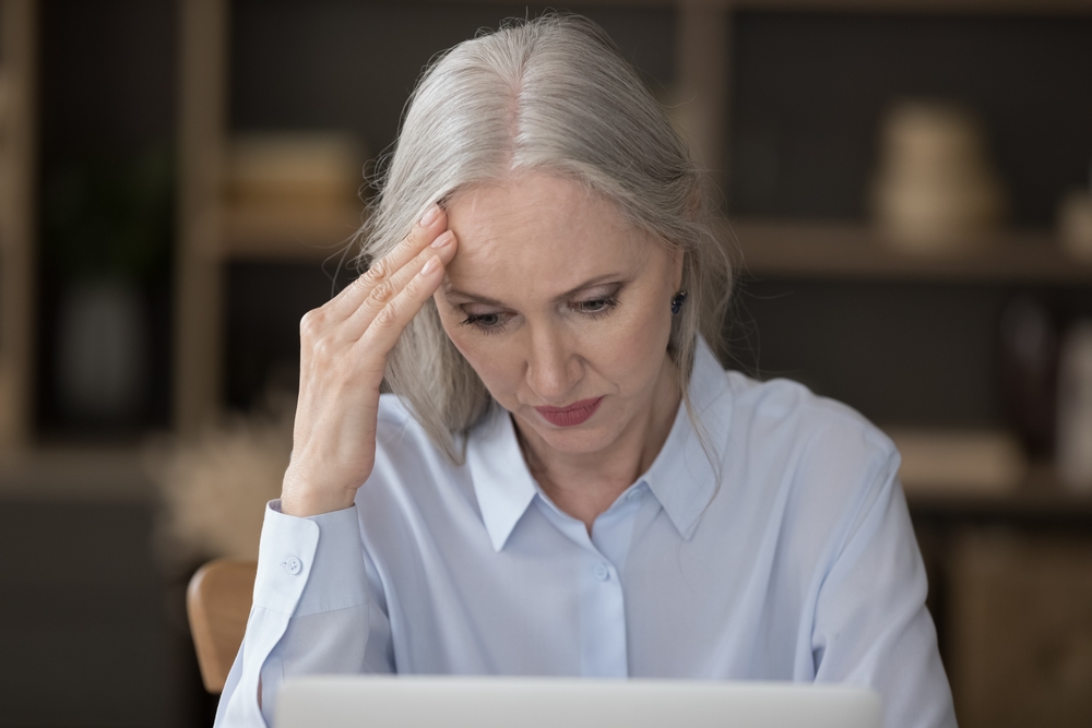 Woman sitting at a desk in front of a laptop holding her hand to her head in concern