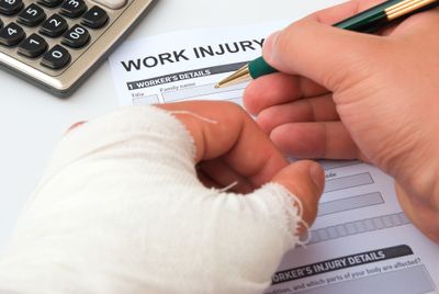 A man with an injured bandaged hand completing a work injury claim form