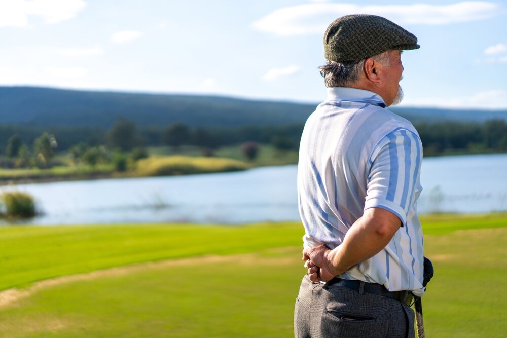 An elderly man presses his first against his lower back, while standing on a golfing green.