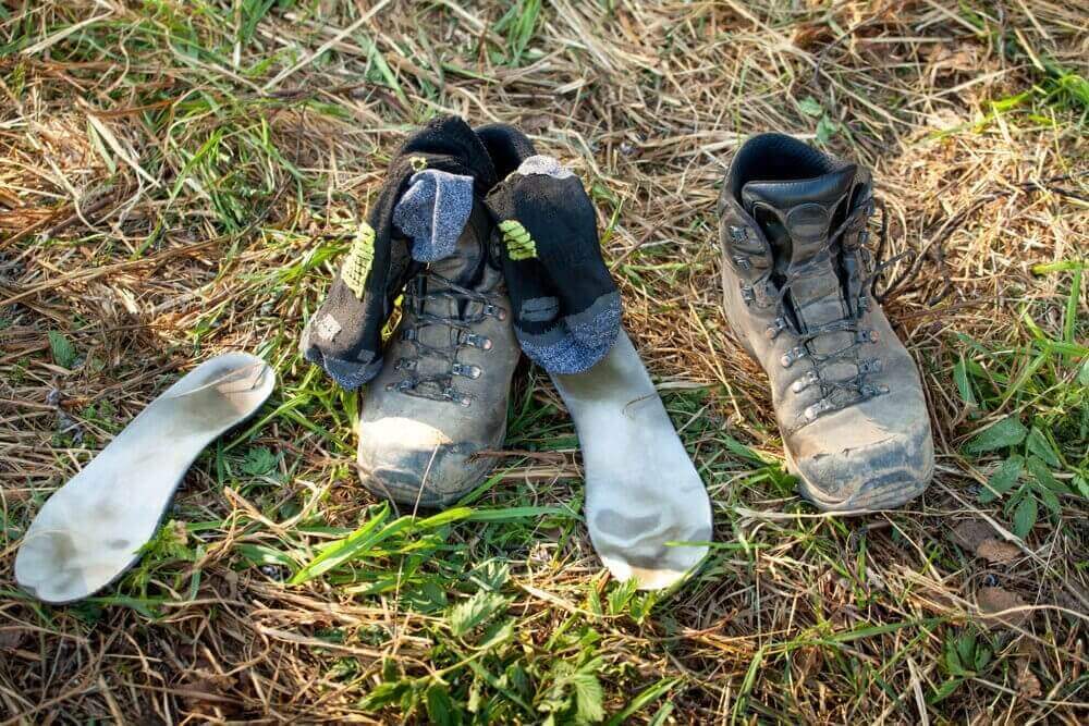 A pair of hiking boots, socks, and insoles drying outside on grass.