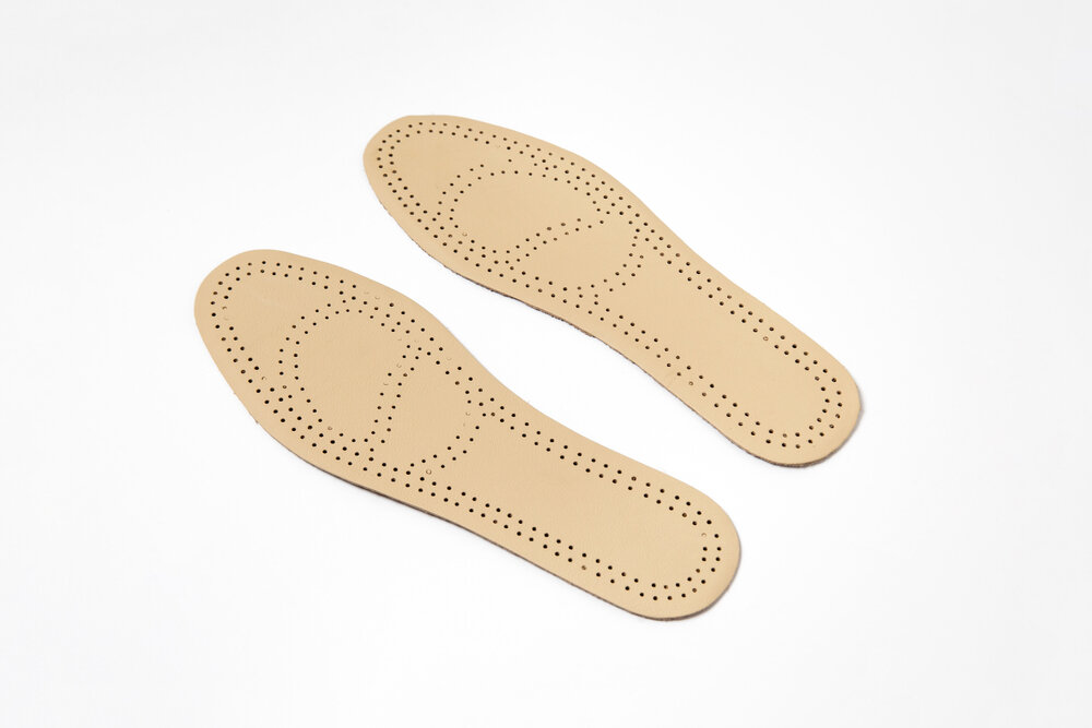 A pair of leather insoles laying against a white background.