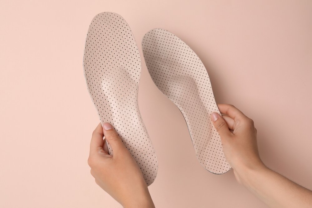 A person holding a pair of insoles up against a light pink background.