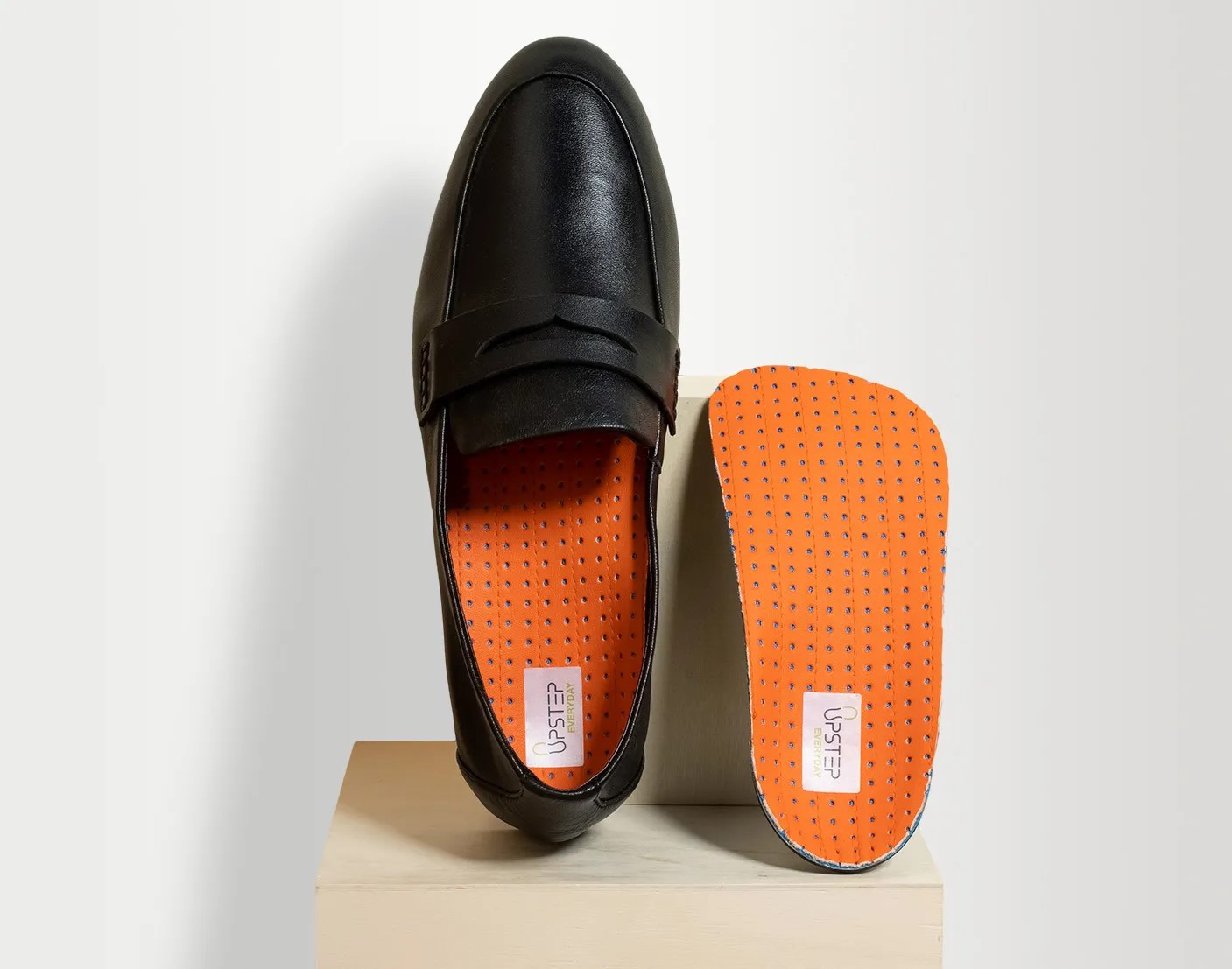 Orange Upstep insoles for heel pain being displayed vertically in and next to a formal shoe