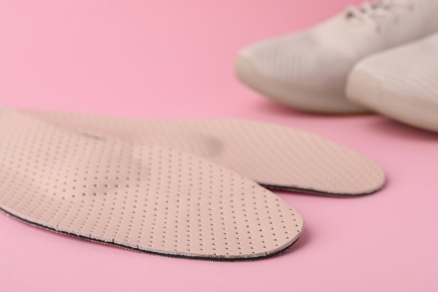 Light pink  orthopedic insoles on pink background. White trainers behind them.