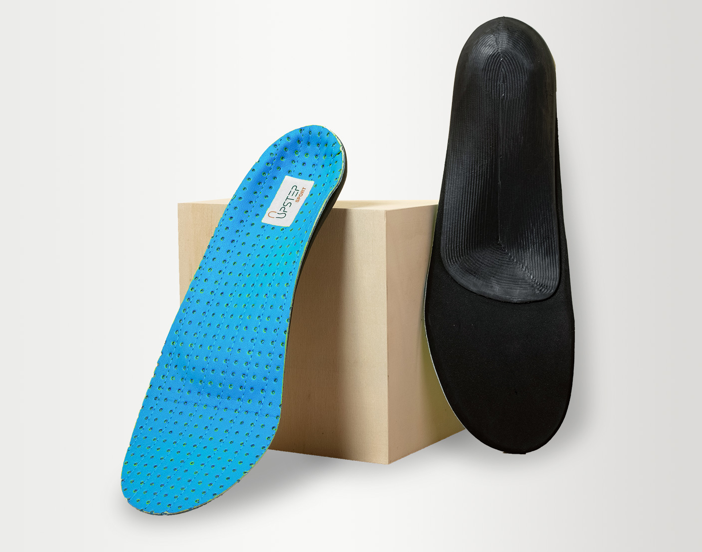 A pair of insoles leaning against a box showcasing the front and back of the insoles