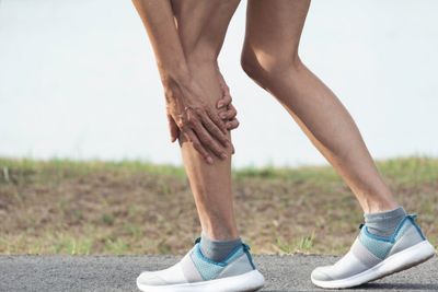 A runner with their hands pressed against the side and back of their left calf.