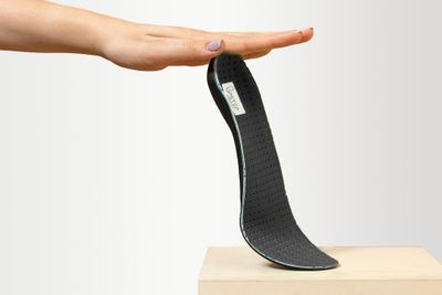 A person holding a black orthotic up, on a wooden pedestal.