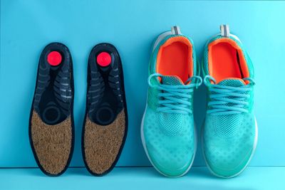 A pair of insoles placed next to a pair of bright blue running shoes, against a blue background.