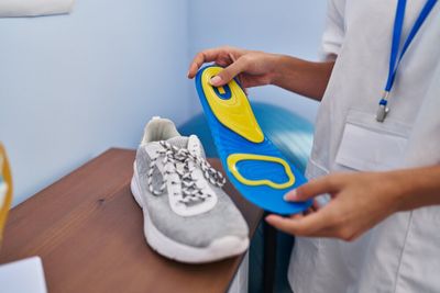 A medical professional holding an orthotic in her hands, with a shoe placed on the counter in front of her.