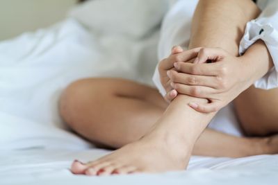 Person sitting on a bed holding their ankle