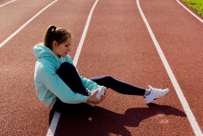 Woman in sports kit sitting on running track and clutching her foot