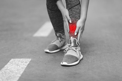 A black and white image of someone holding their shin with painful area highlighted in red