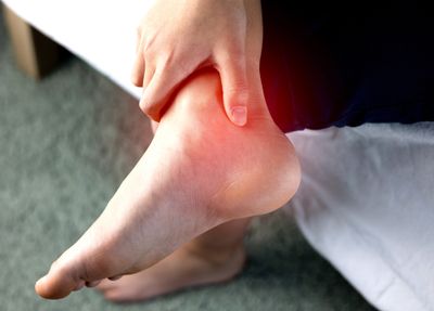 A person holding the back of their heel with a highlighted red area showing where pain is being felt