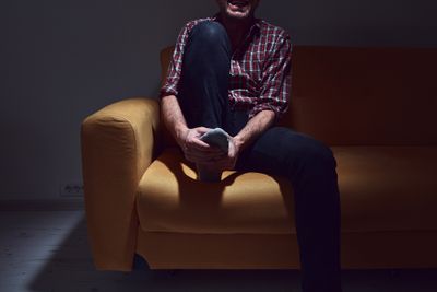 Man in dimly-lit room clutching foot and grimacing while sitting on couch