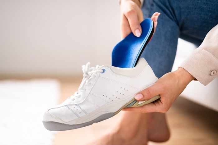 A woman busy placing inserts into white golf shoe.