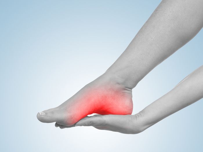 Greyed image of woman rubbing red-highlighted sole of her foot
