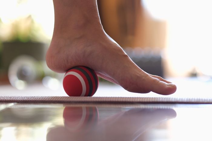 Foot rolling a red ball on a wooden floor