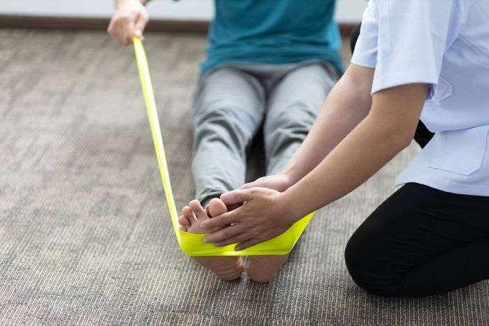 A physical therapist holding their patient's toes as they do exercises with a stretch band.