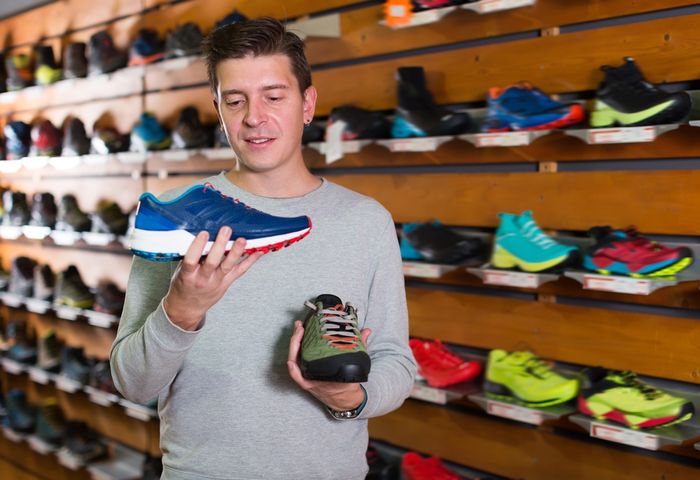 Man holding up different running shoes in sports store
