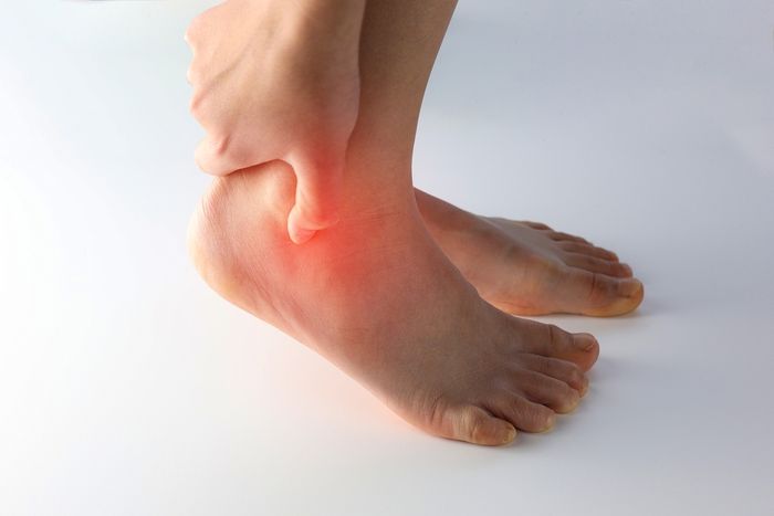 A person holding their ankle with redness showing the area of pain 