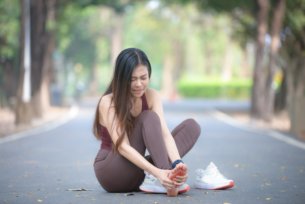 Young woman holding foot with shoe off on the street while wearing exercise gear