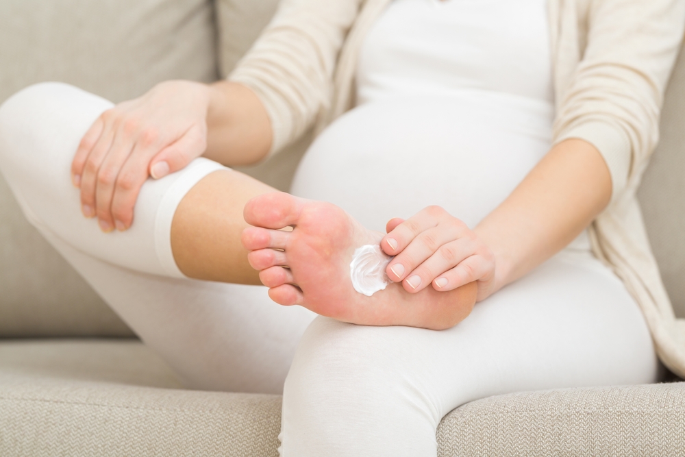 A pregnant woman applying cream to the sole of her foot
